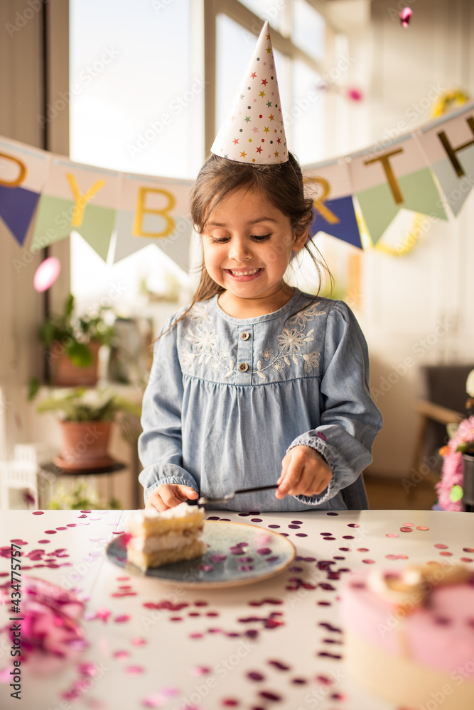 Wall mural girl eating her birthday cake with happy smile at the birthday party at home