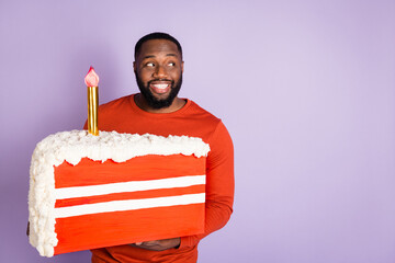 Portrait of attractive cheerful guy holding big fake candle cake look aside copy space isolated...