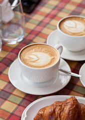 Cups of cappuccino coffee with croissant in a cafe
