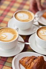 Cups of cappuccino coffee with croissant in a cafe