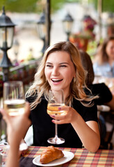 Young woman drinking a white wine in a cafe terrace with friends and laughs