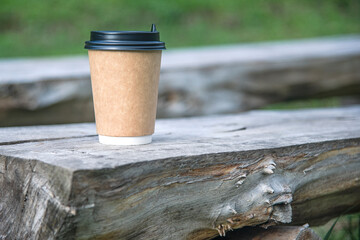 Close-up paper cup of coffee on natural background on a wooden bench. For a coffee shop