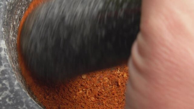 Close-up of the pestle mixing spices and peppers in the stone mortar