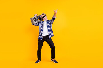 Full size photo of happy excited crazy mature man hold boombox on shoulder relaxing isolated on yellow color background