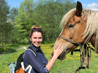 A woman plays with a horse. The horse is grazing in the spring meadow. Close-up shot of a horse's head.