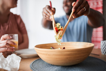 Man mixing salad with wooden spoons while preparing dinner