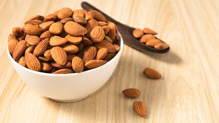 Almond nuts in a white bowl on wooden background, selective focus.front view.copy space.