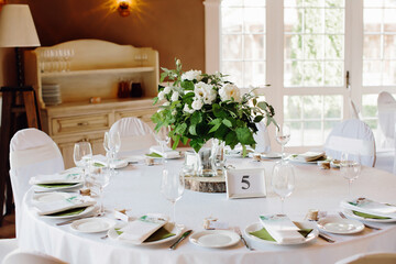 Festive table setting in white colors, at a dinner dedicated to a wedding or birthday. Round table with personalized seating cards. Selective focus.