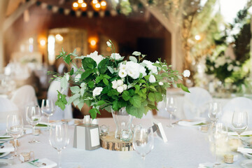 Bouquet of white flowers with greenery, as table decoration for festive dinner. Celebration in honor of wedding or birthday. Selective focus.