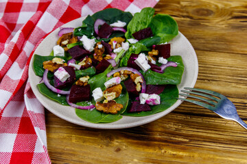 Tasty spinach salad with boiled beetroot, feta cheese, walnut and red onion on wooden table. Healthy vegetarian food