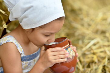 Portrait of a beautiful little girl with milk in field at summer