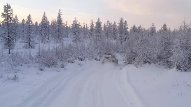 The six-wheel Trekol all-terrain vehicle rides through the snow-covered tundra in the sunset light
