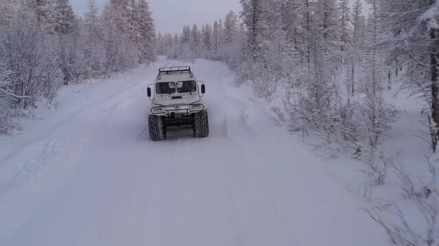 The six-wheel Trekol all-terrain vehicle rides through the snow-covered tundra in the sunset light

