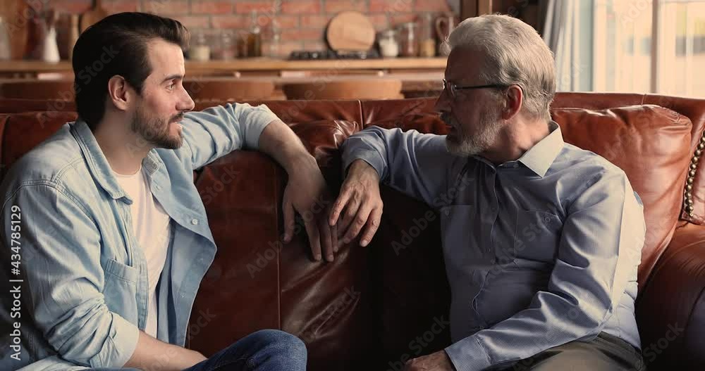 Wall mural older man his grown up millennial son sit on sofa and talking, share news enjoy moments together hav