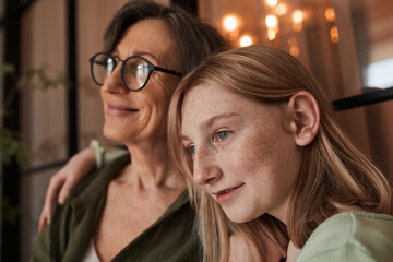 Girl bonding to her senior grandmother and looking away while enjoying