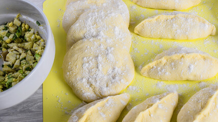 Raw homemade pies stuffed with egg and onion, on the kitchen table. Concept of making pies at home. Top and side view. Selective focus.