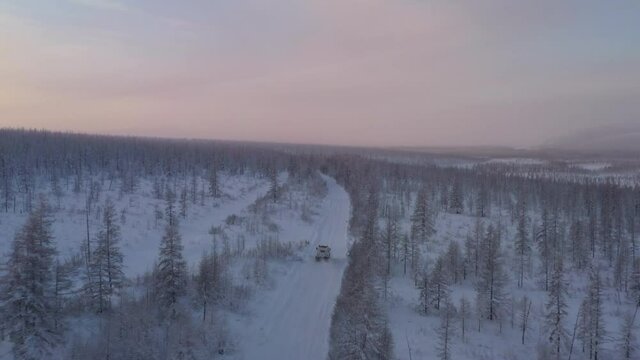 The six-wheel Trekol all-terrain vehicle rides through the snow-covered tundra in the sunset light

