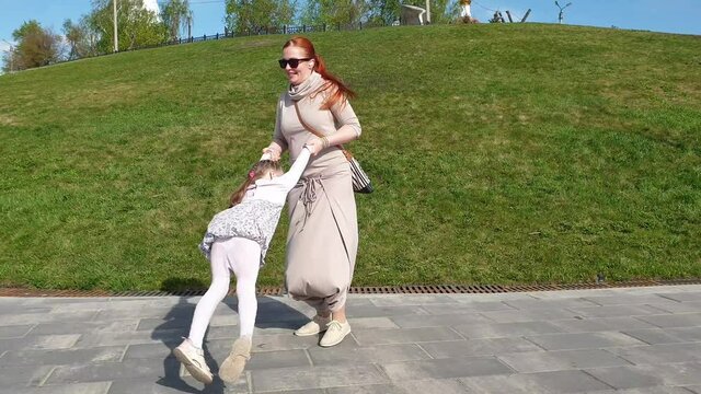mom twirls her little daughter by the hands, a woman plays with a child in the park