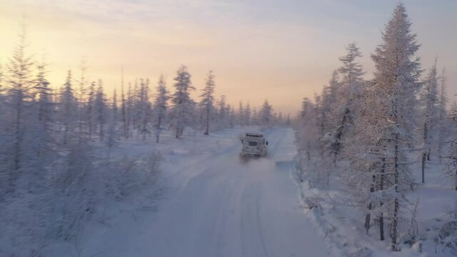 The six-wheel Trekol all-terrain vehicle rides through the snow-covered tundra in the sunset light
