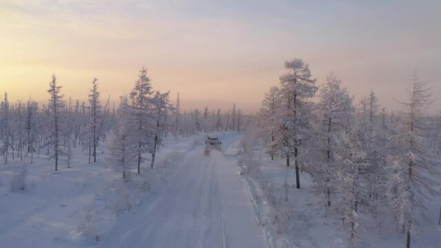The six-wheel Trekol all-terrain vehicle rides through the snow-covered tundra in the sunset light
