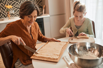 Woman chopping with the knife fresh dough while baking bagels with her granddaughter