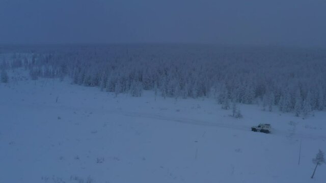 The six-wheel Trekol all-terrain vehicle rides through the snow-covered tundra in the sunset light
