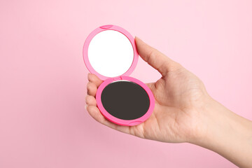 Woman holding stylish cosmetic pocket mirror on pink background, closeup