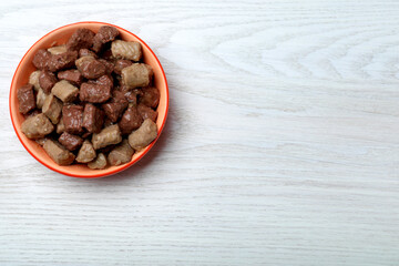 Wet pet food in feeding bowl on white wooden table, top view. Space for text