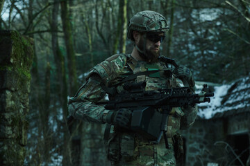 Fototapeta premium Portrait of airsoft player in professional equipment with machine gun in the forest. Soldier with weapons at war