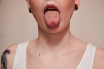 Extravagant woman with piercing at her face showing her tongue while posing