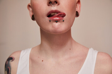 Woman having nude makeup and tattoos standing in front of the camera and showing her tongue