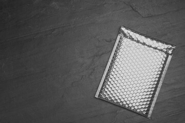Padded envelope with bubble wrap on black background, top view. Space for text