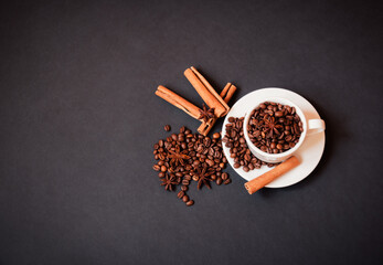 Coffee cup with roasted coffee beans and spices on dark background.