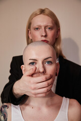 Man standing behind the bald masculine woman and hiding her mouth