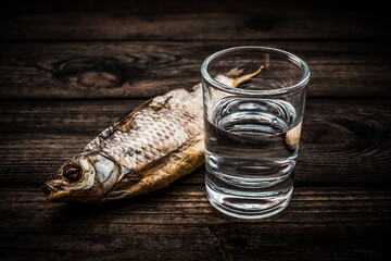 Shot of vodka with a stockfish on an old wooden table. Close up view