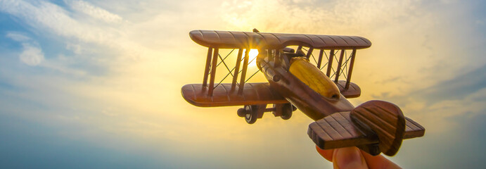 The hand with a wooden airplane on the background of the sunset
