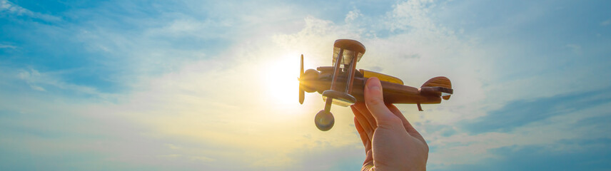 The hand with a wooden airplane on the background of the sunset