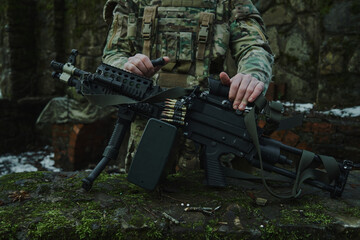 Portrait of airsoft player in professional equipment loads a gun with bullets in the forest. Soldier with weapons at war