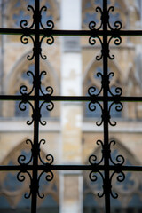 London, UK - February 4, 2017:  Artistic view of gothic iron gate juxtaposed with cathedral windows blurred in background. Unique perspective