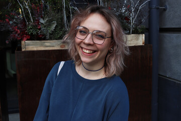 Fototapeta premium Young woman in square retro glasses smiles broadly. Natural beauty without gloss. Walk in the gorola. Emotional person laughing