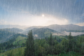 Naklejka premium Rain and sun through the clouds over the green summer Carpathian foggy mountain hills. Rainy evening panorama.