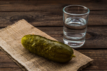 Shot of vodka with piece of cloth and pickled cucumber on an old wooden table. Close up view