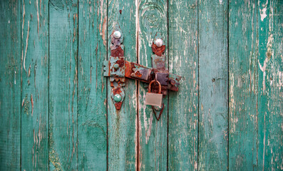 Old wooden gate with a rusty barn lock on a green background