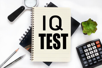 IQ test (Intelligence quotient ). an open notebook lies on a closed notebook near a calculator and a magnifying glass on a white workspace.