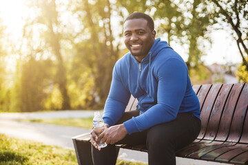 Man resting on bench after exercise and  drinking water . - obrazy, fototapety, plakaty