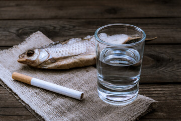 Shot of vodka with a stockfish and a piece of cloth with cigarette on an old wooden table. Close up view