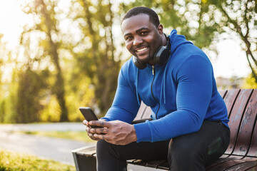Fototapeta premium Man with headphones using mobile phone while resting after exercise on bench.