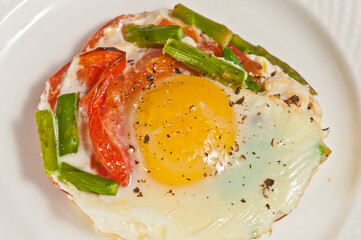 top view, close up of, asparagus, sunny side up egged tomato tart, with ground pepper, on a round, white plate