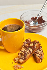 top, front view of three peanut butter oatmeal biscotti's with dribbled chocolate on yellow plate, yellow cup of espresso and bowl of chocolate with spoon