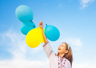 Fototapeta premium a girl in Ukrainian embroidered shirt holds blue and yellow balloons